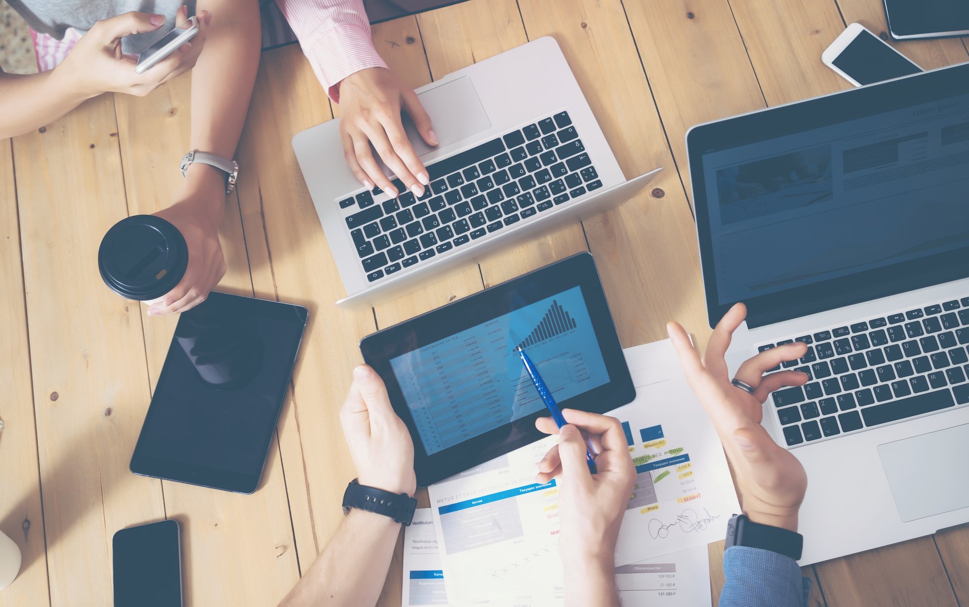 Generisches B&uuml;ro, mehrere H&auml;nde die &uuml;ber einen Tisch greifen Laptops und Tablets auf dem tisch
