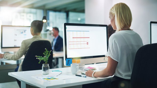 Generische Officeszene: Frau sitzt vor Bildschirm Kachel Vorschau